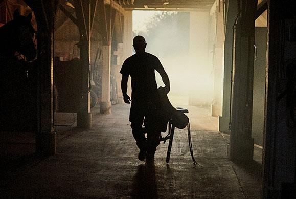 silhouette of war veteran holding saddle walking through barn